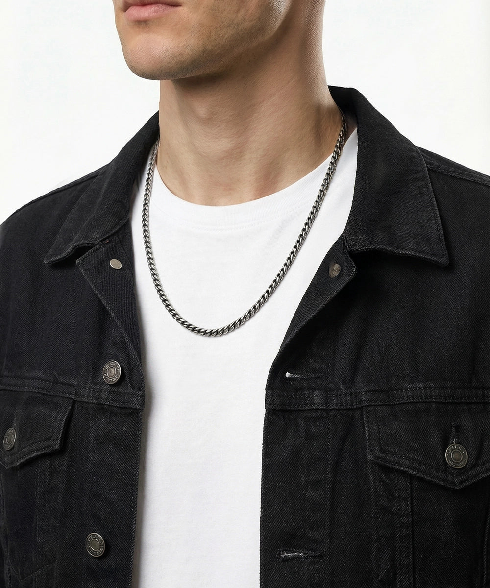 Person wearing a black denim jacket and white shirt with a chain necklace.