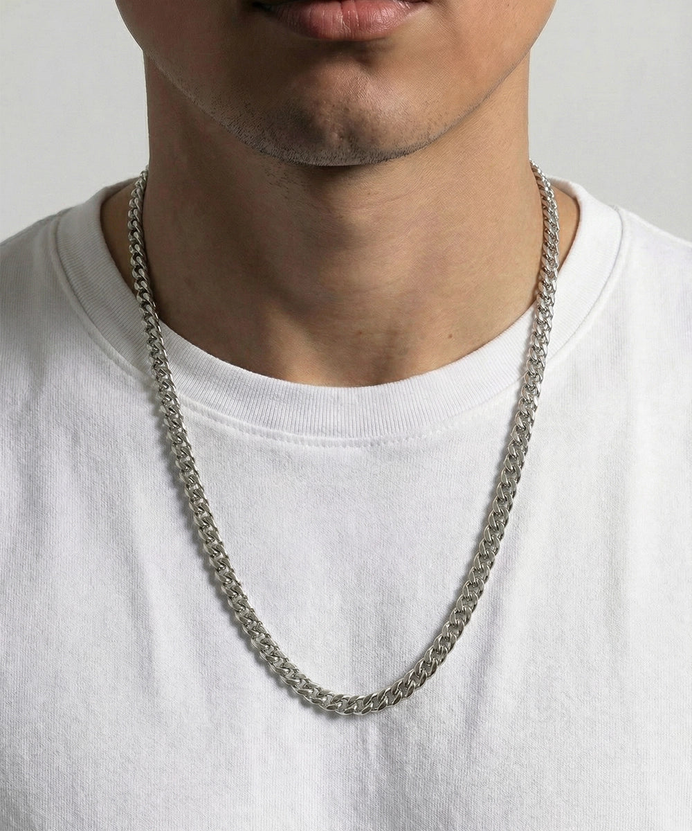 Person wearing a silver chain necklace on a plain background