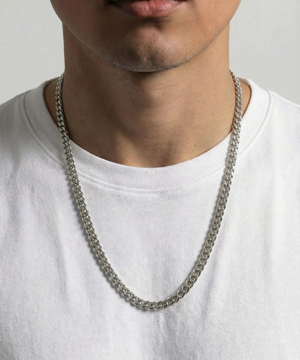 Person wearing a silver chain necklace on a plain background