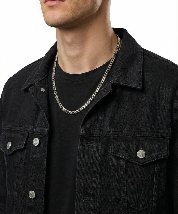 Person wearing a black denim jacket and black shirt with a silver chain necklace.