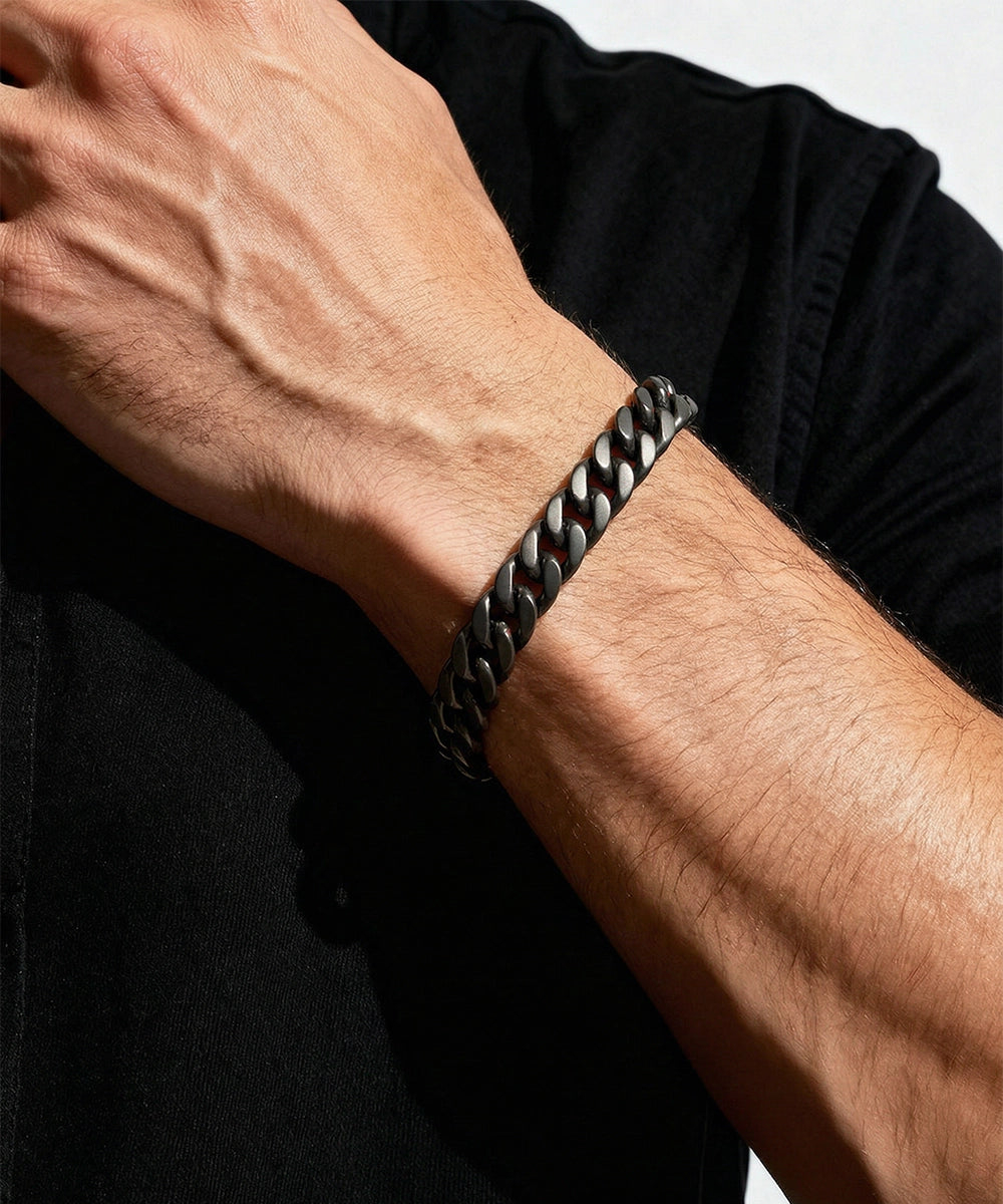 Person wearing a black braided bracelet on a plain background