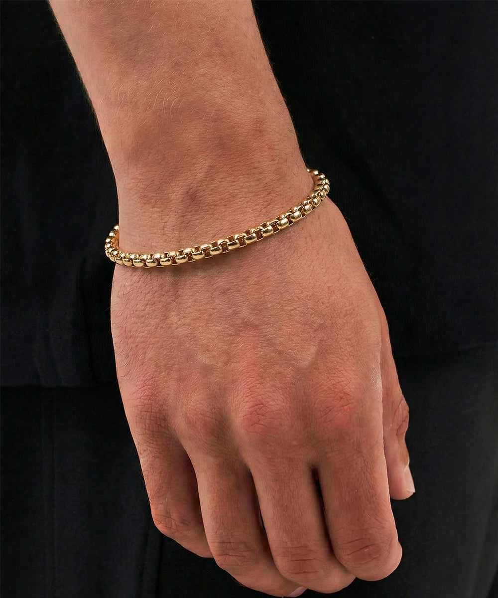 Gold chain bracelet on a person's wrist against a black background