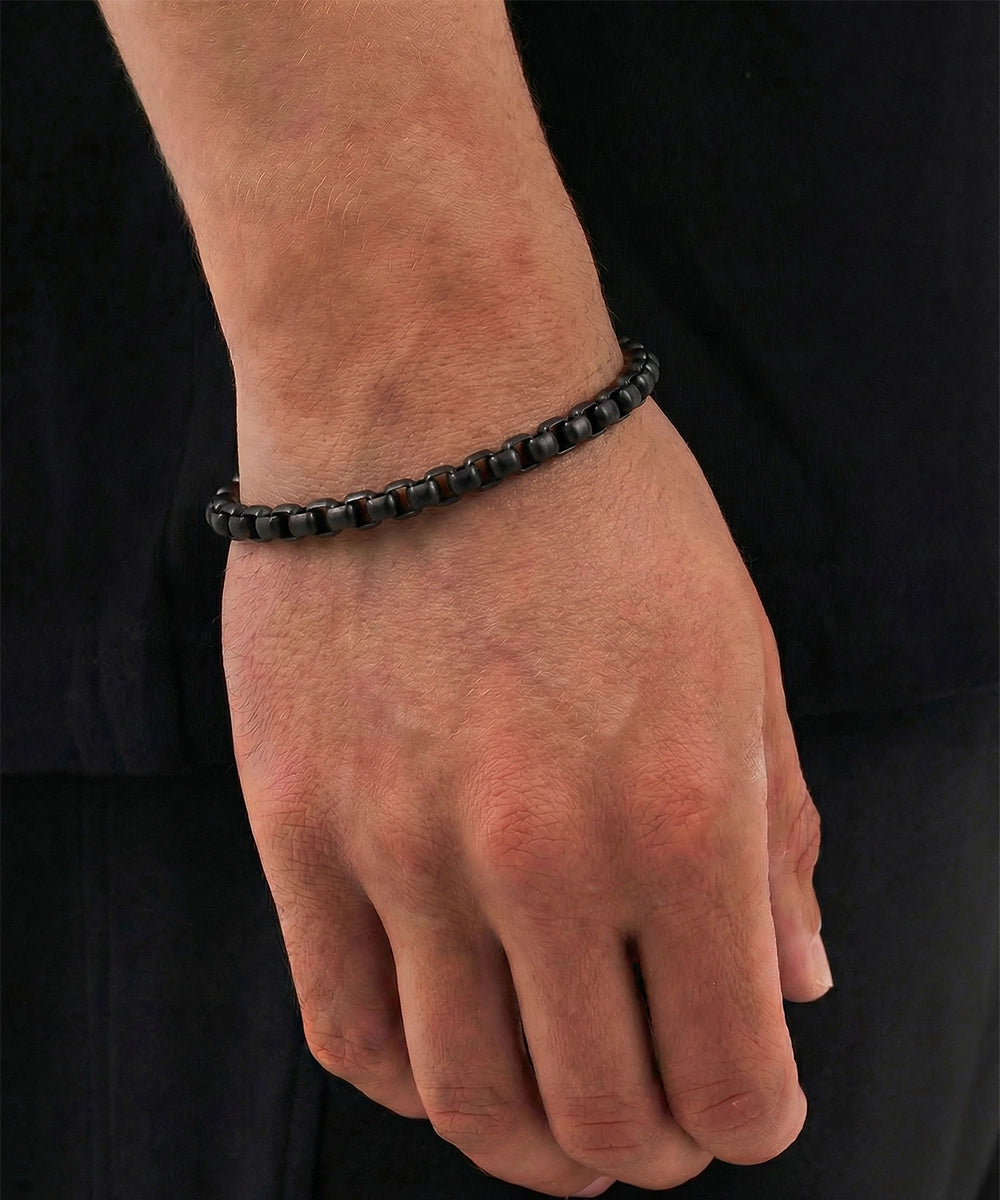 Hand wearing a black beaded bracelet against a black background