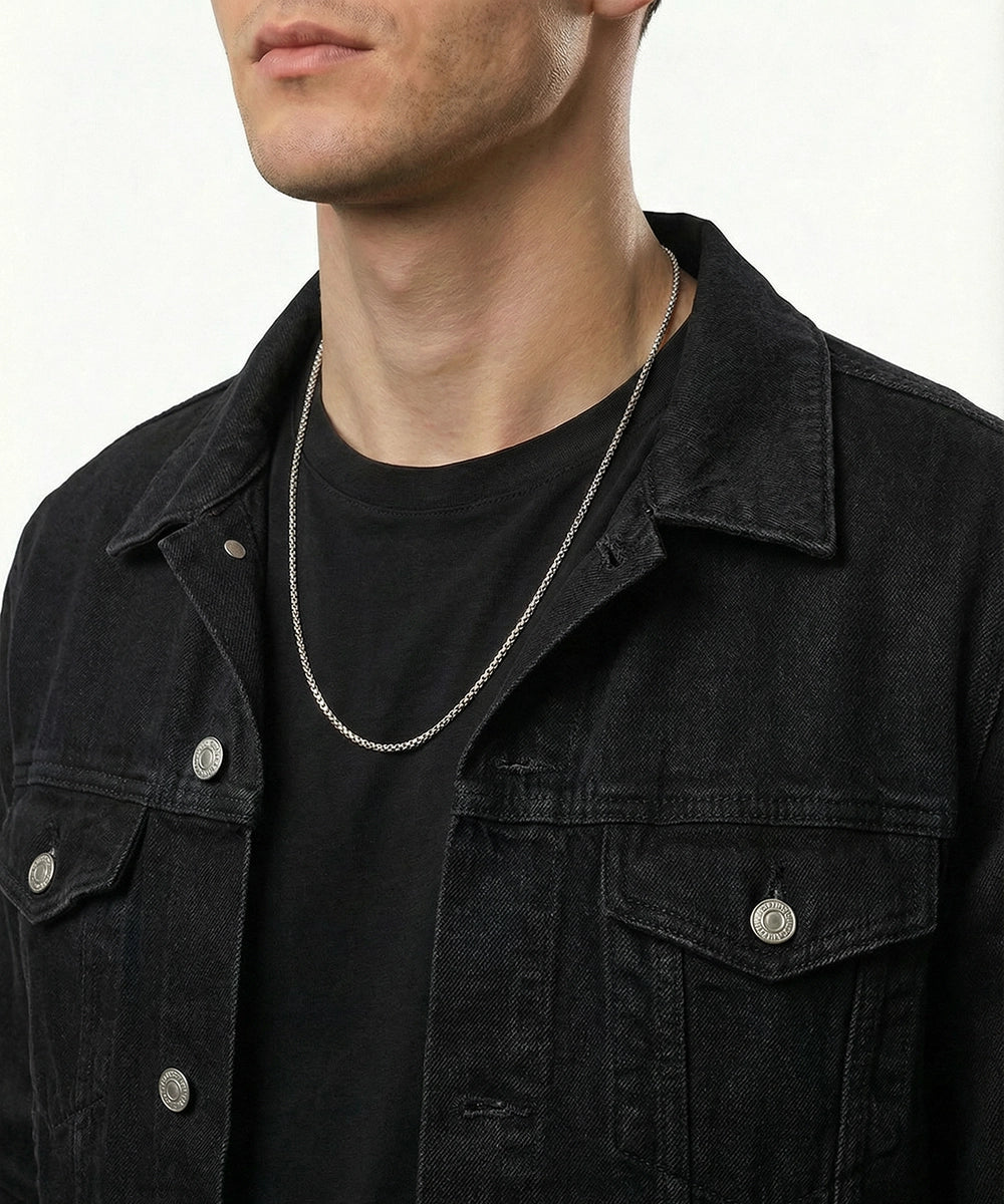 Man wearing a black denim jacket and black shirt with a silver chain necklace.
