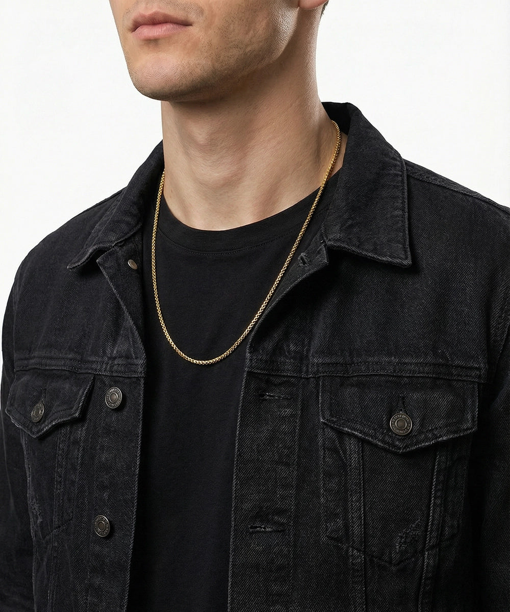 Man wearing a black denim jacket and gold chain necklace on a white background