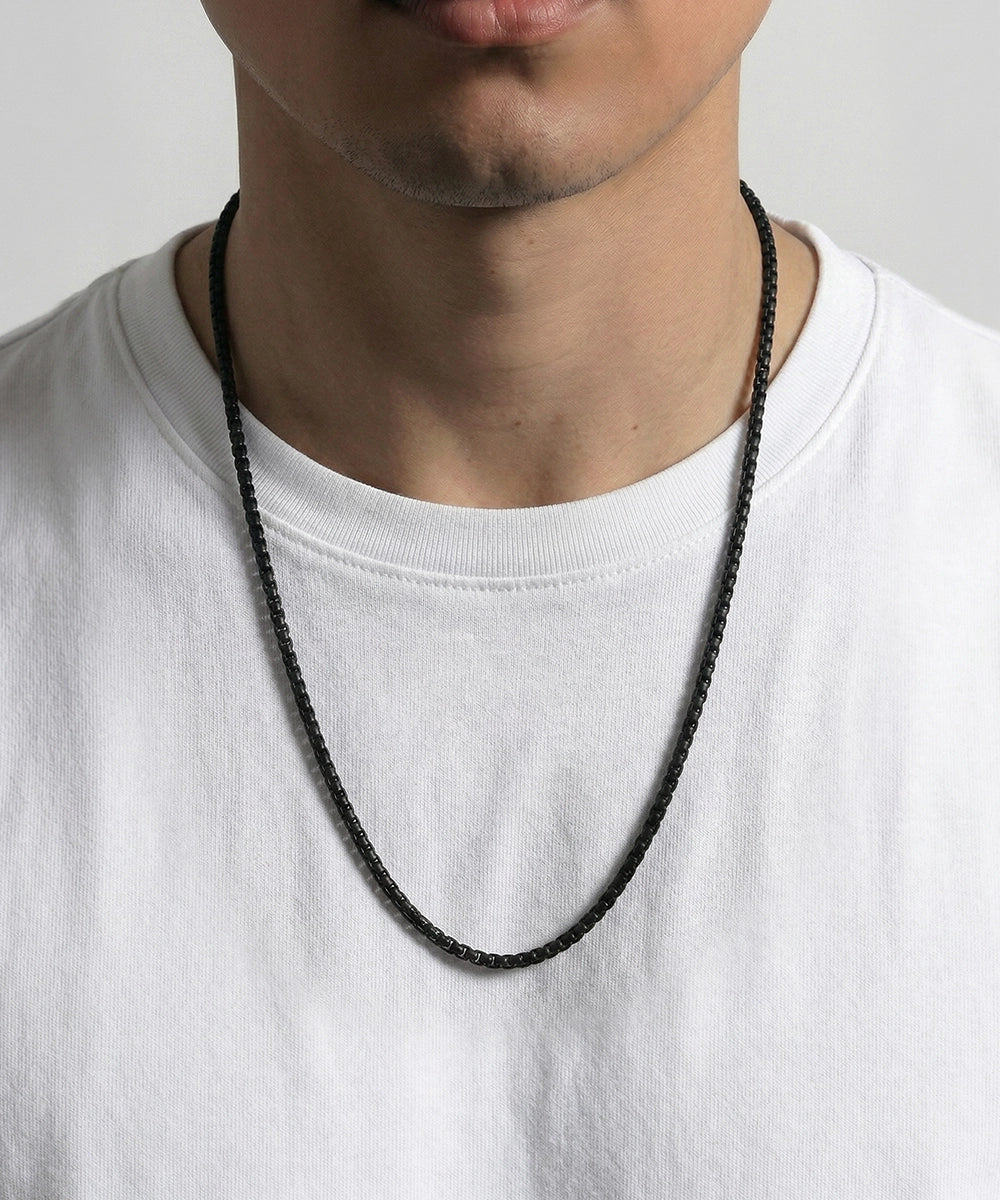 Person wearing a black necklace against a plain background