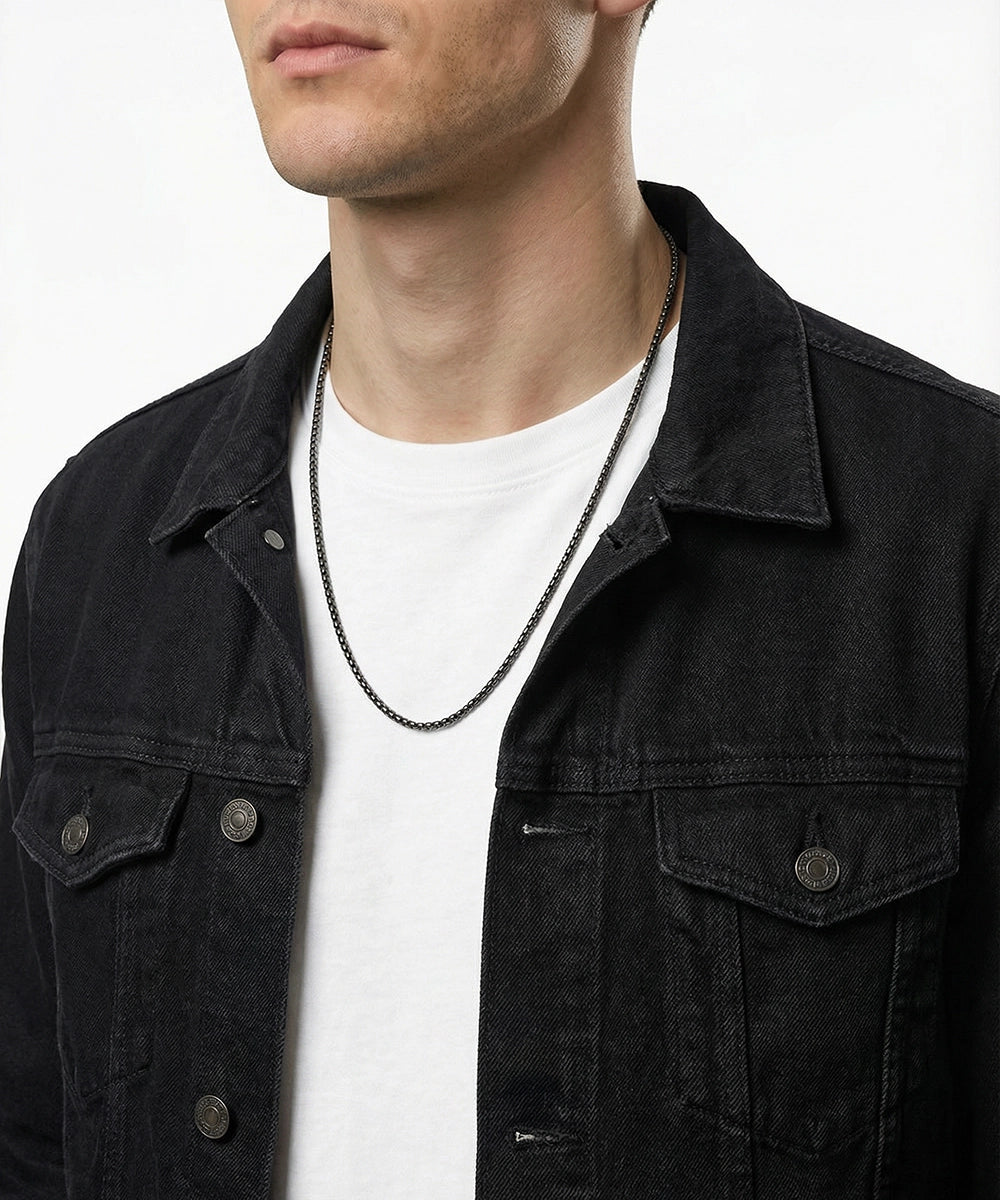 Man wearing a black denim jacket over a white shirt with a necklace.