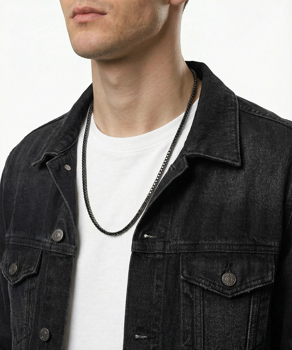 Person wearing a black denim jacket and white shirt with a necklace.