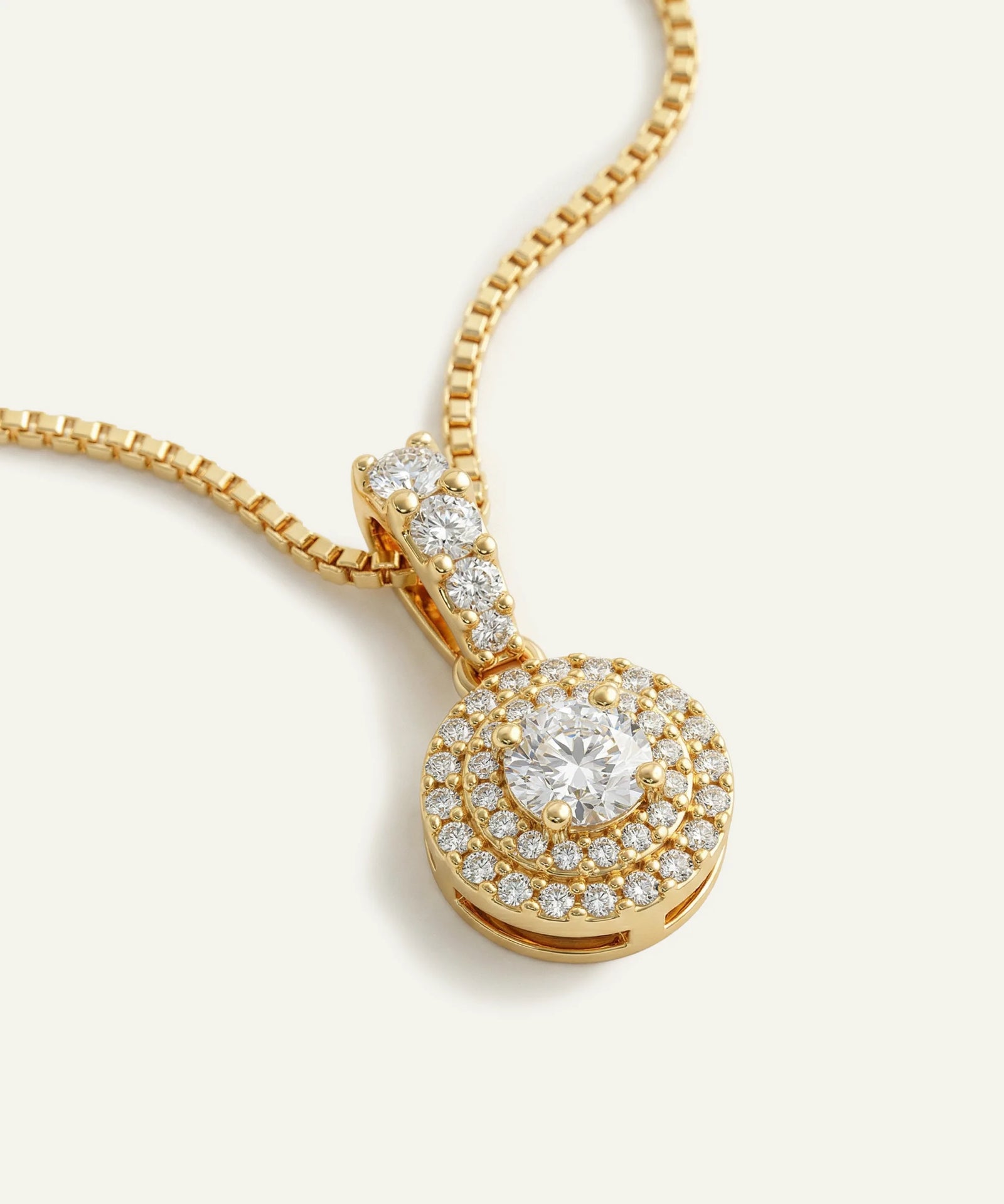 Gold necklace with a diamond pendant on a light beige background