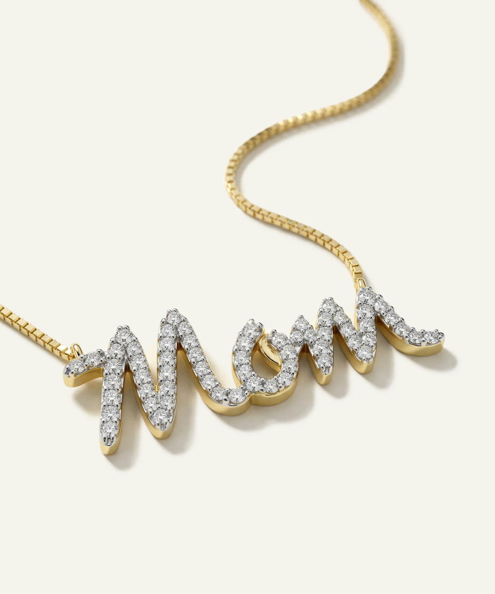 Gold necklace with 'MOM' pendant on a light background