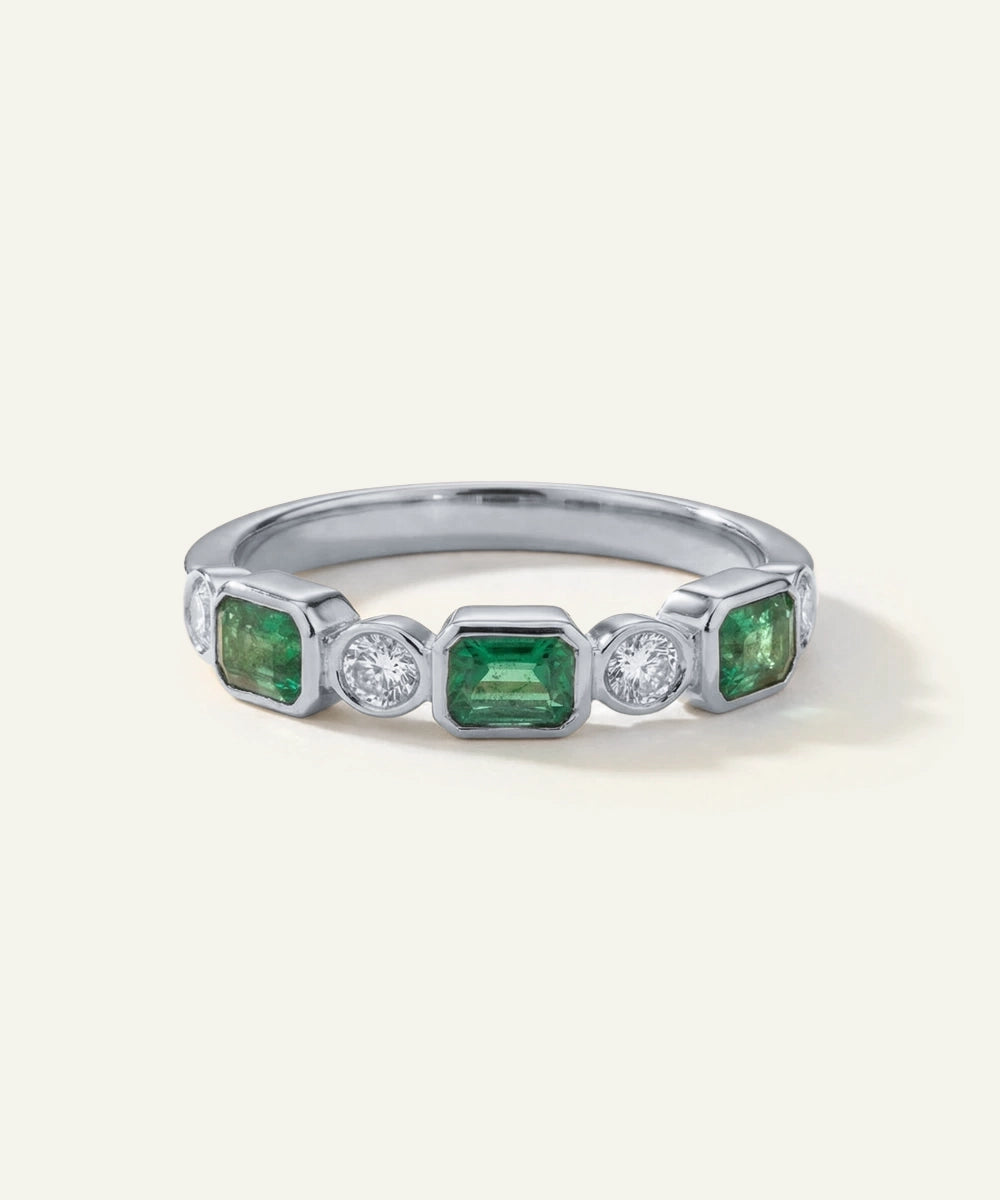 Silver ring with green gemstones and clear stones on a white background