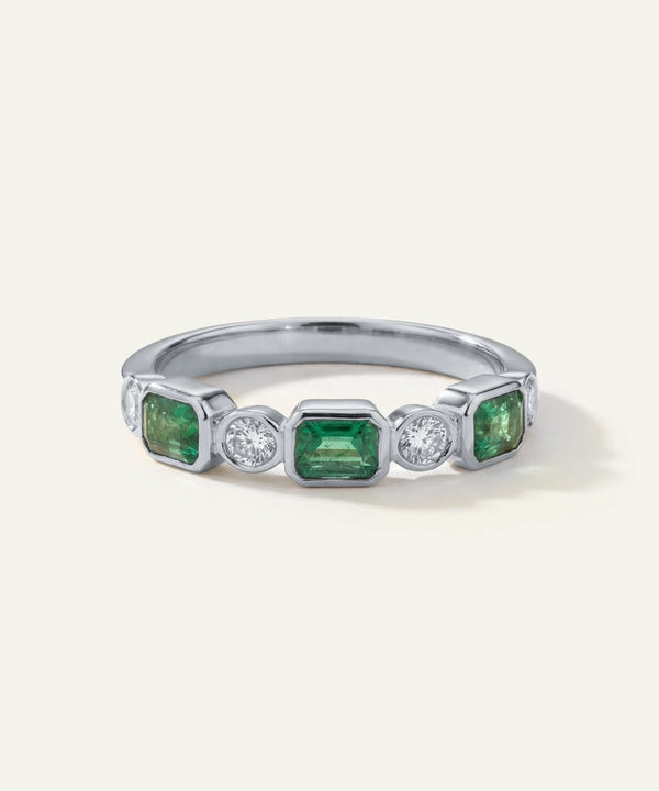Silver ring with green gemstones and clear stones on a white background