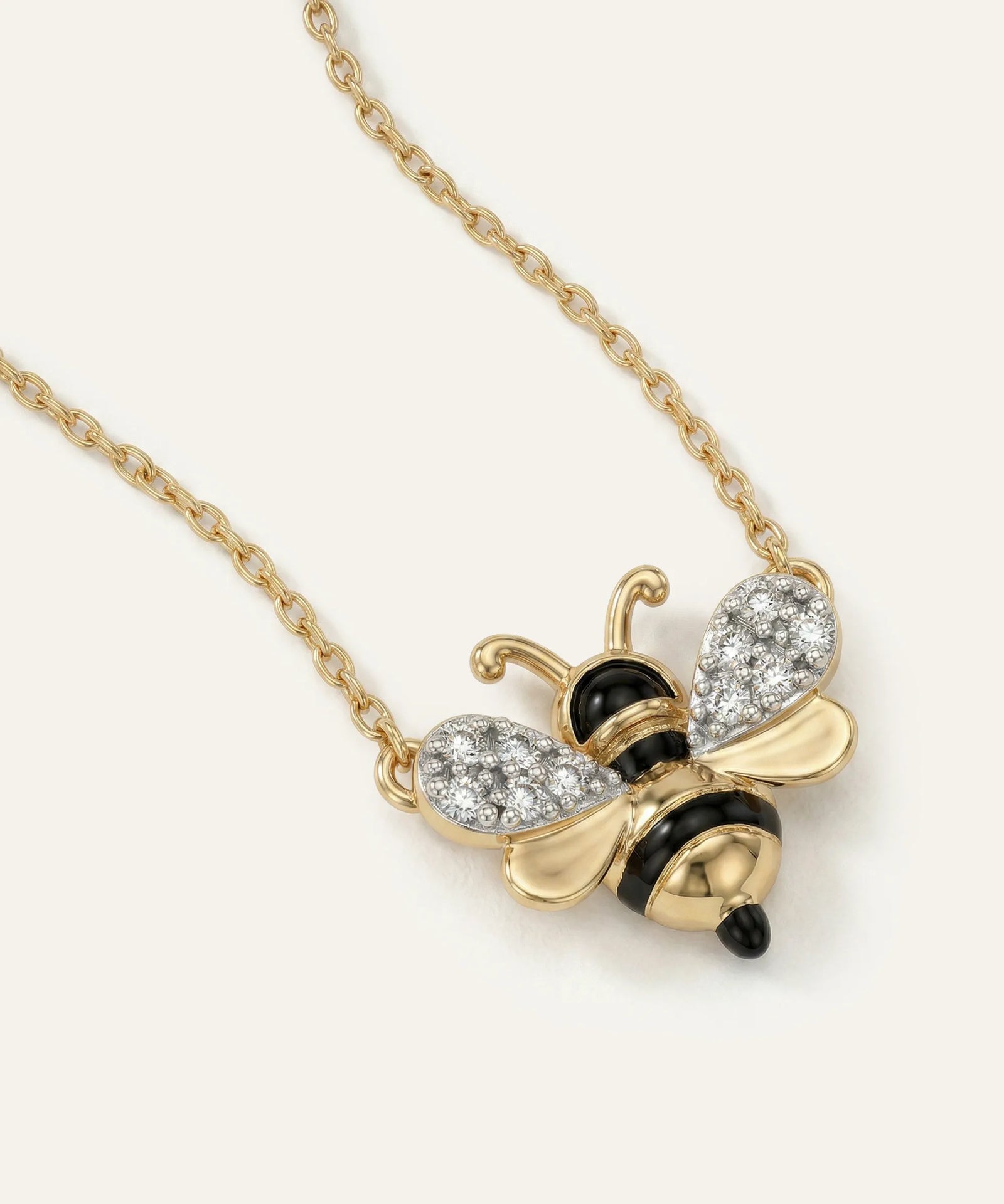 Gold bee-shaped necklace with black and white accents on a light beige background