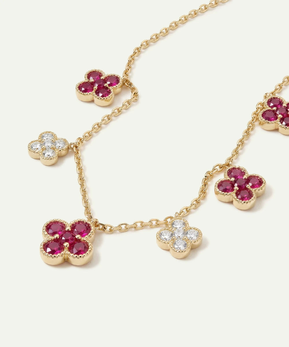 Gold necklace with ruby and diamond flower pendants on a white background