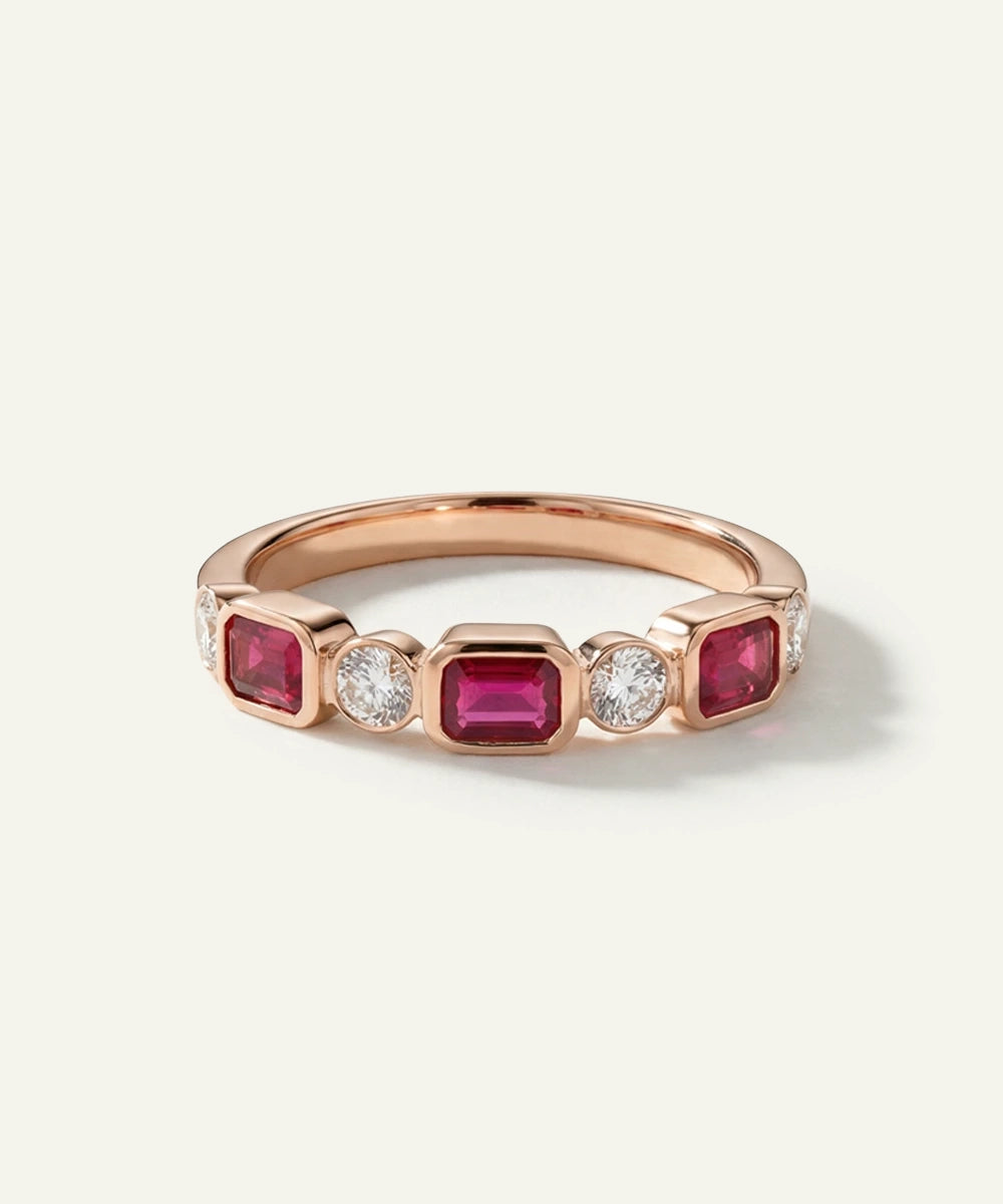 Rose gold ring with red gemstones and a diamond on a light gray background