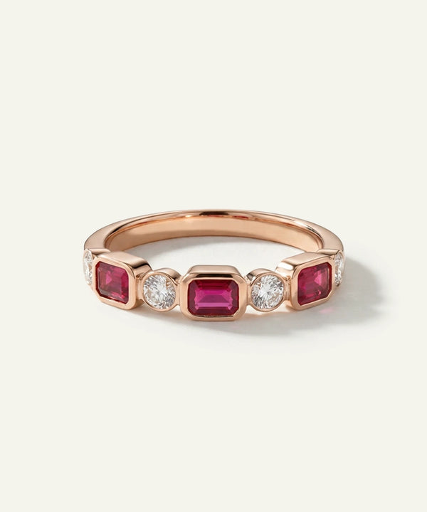 Rose gold ring with red gemstones and a diamond on a light gray background