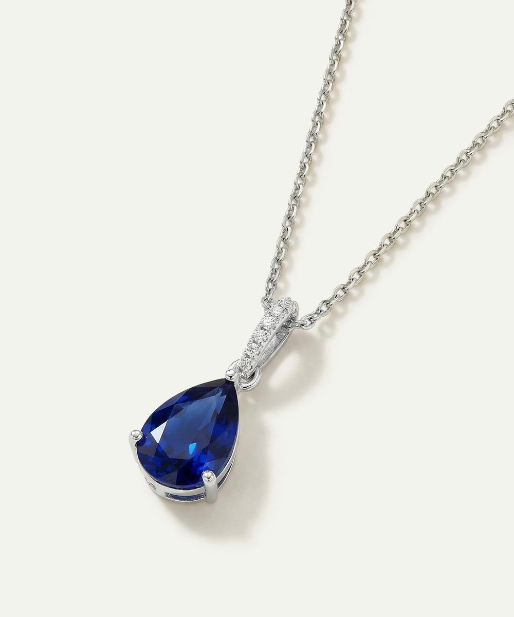 Teardrop-shaped blue gemstone pendant on a silver chain against a white background