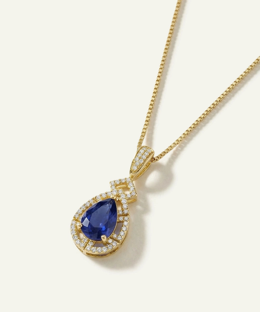Gold necklace with a blue teardrop pendant on a white background