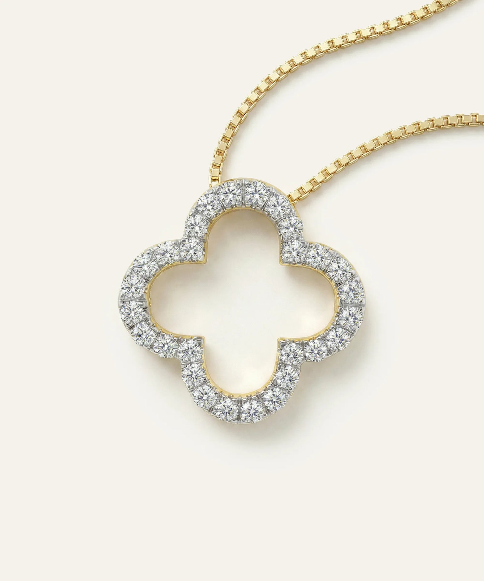 Diamond-studded clover-shaped pendant on a gold chain against a white background