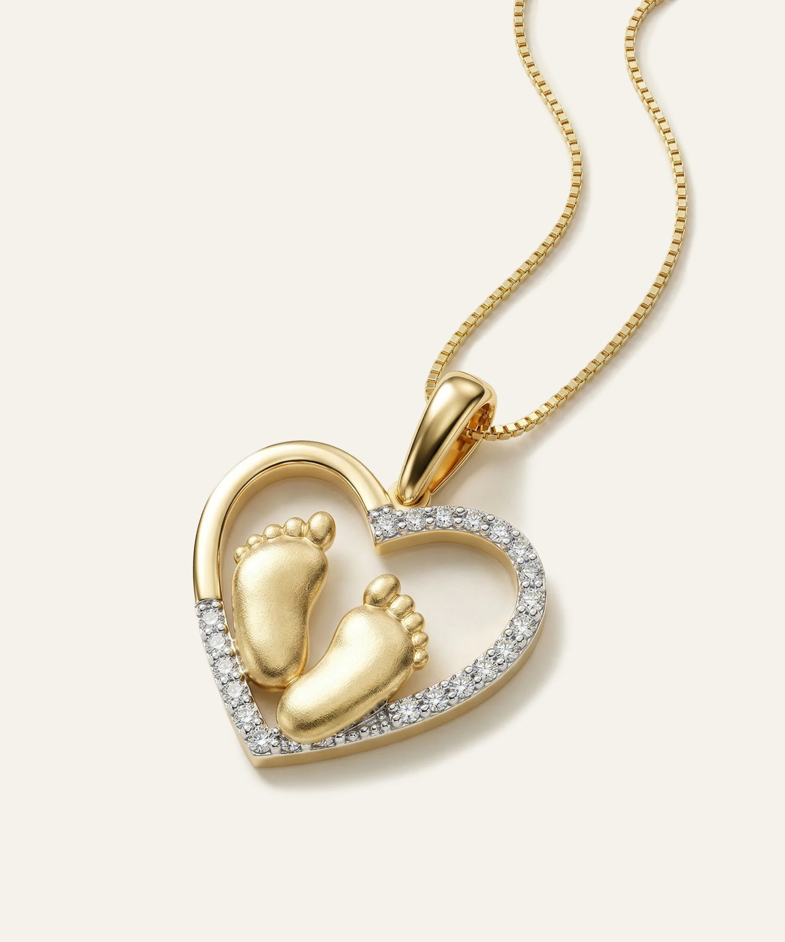 Gold heart-shaped pendant with baby feet design on a white background