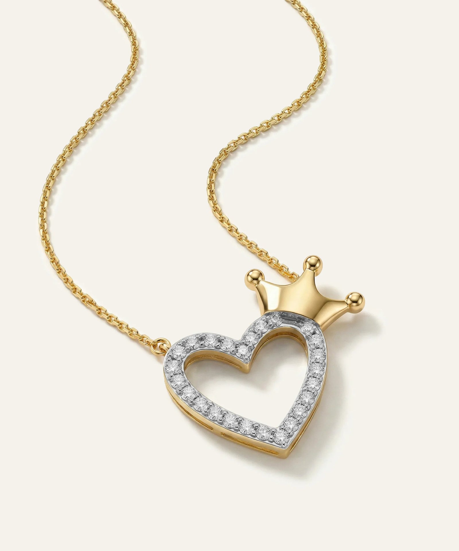 Gold necklace with a heart-shaped pendant featuring a crown on a light beige background