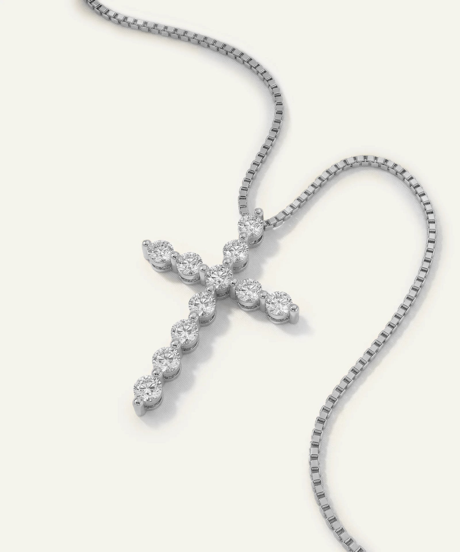 Diamond cross pendant on a chain against a white background