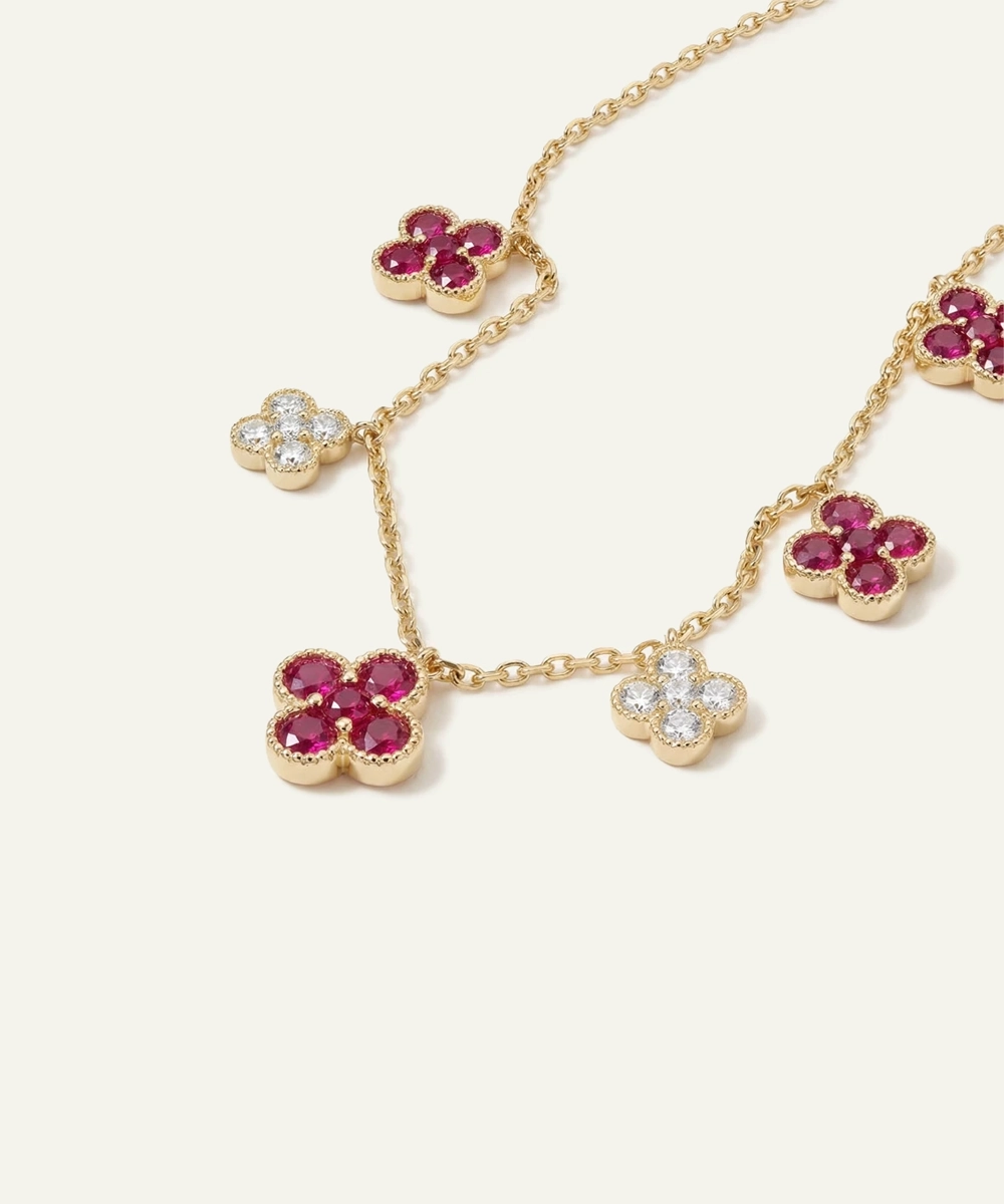 Gold necklace with floral pendants featuring red stones and clear gemstones on a white background
