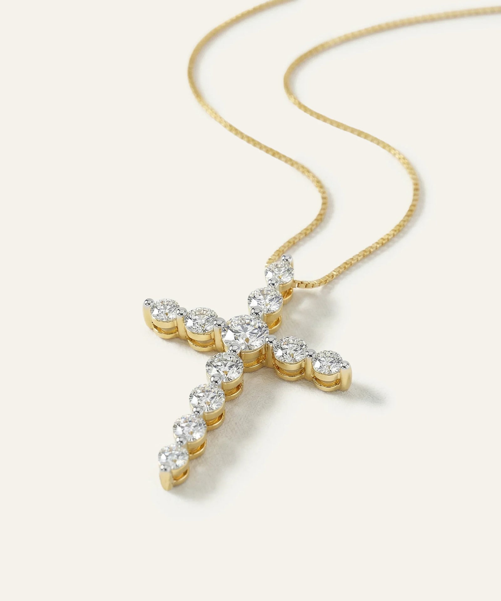 Gold cross necklace with diamonds on a light beige background