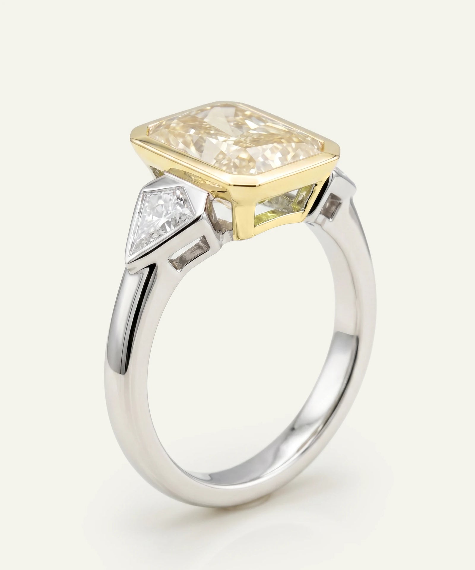 Two-tone diamond ring with a large central diamond and smaller side stones on a white background