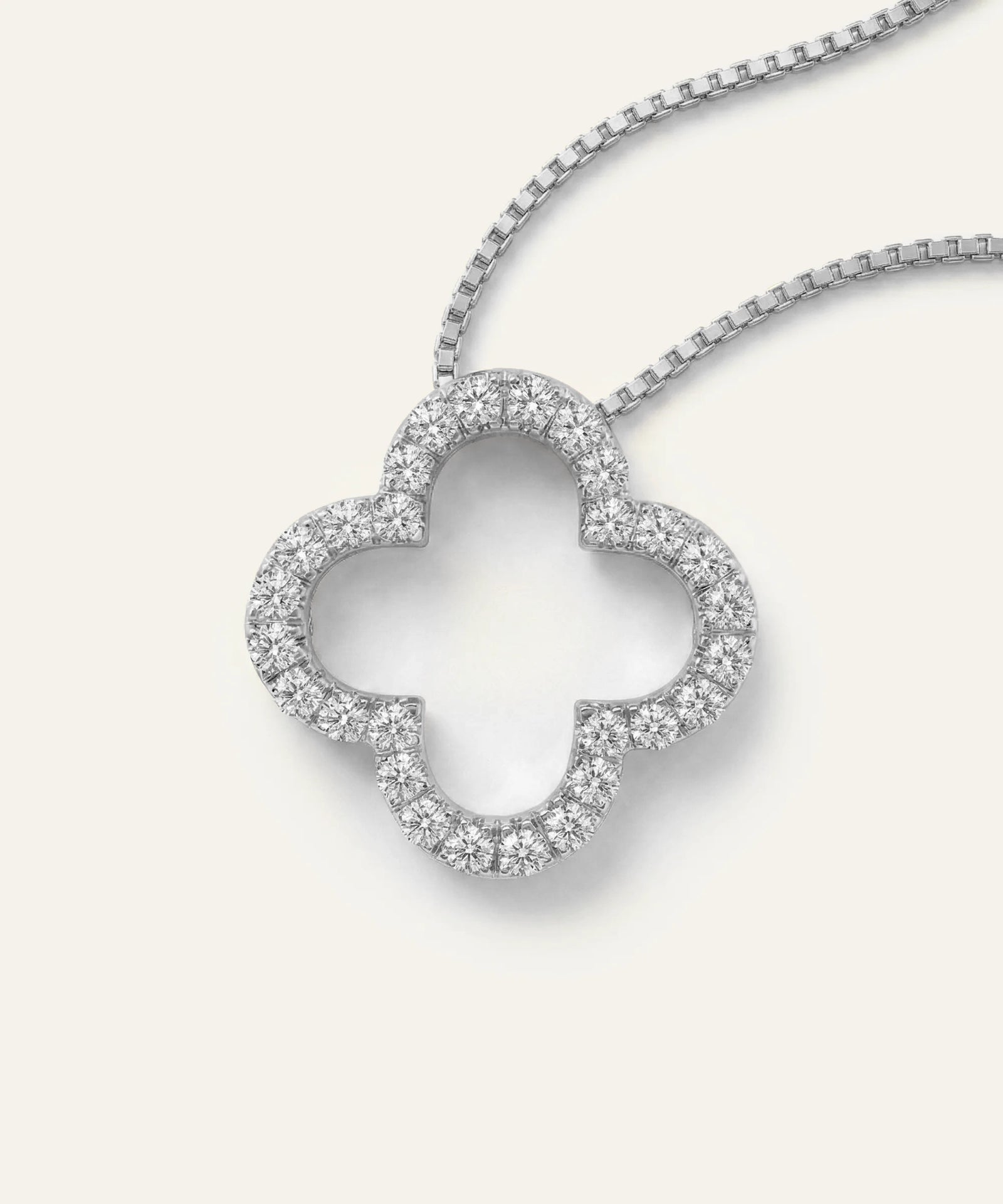 Diamond-studded clover-shaped pendant on a chain against a light gray background