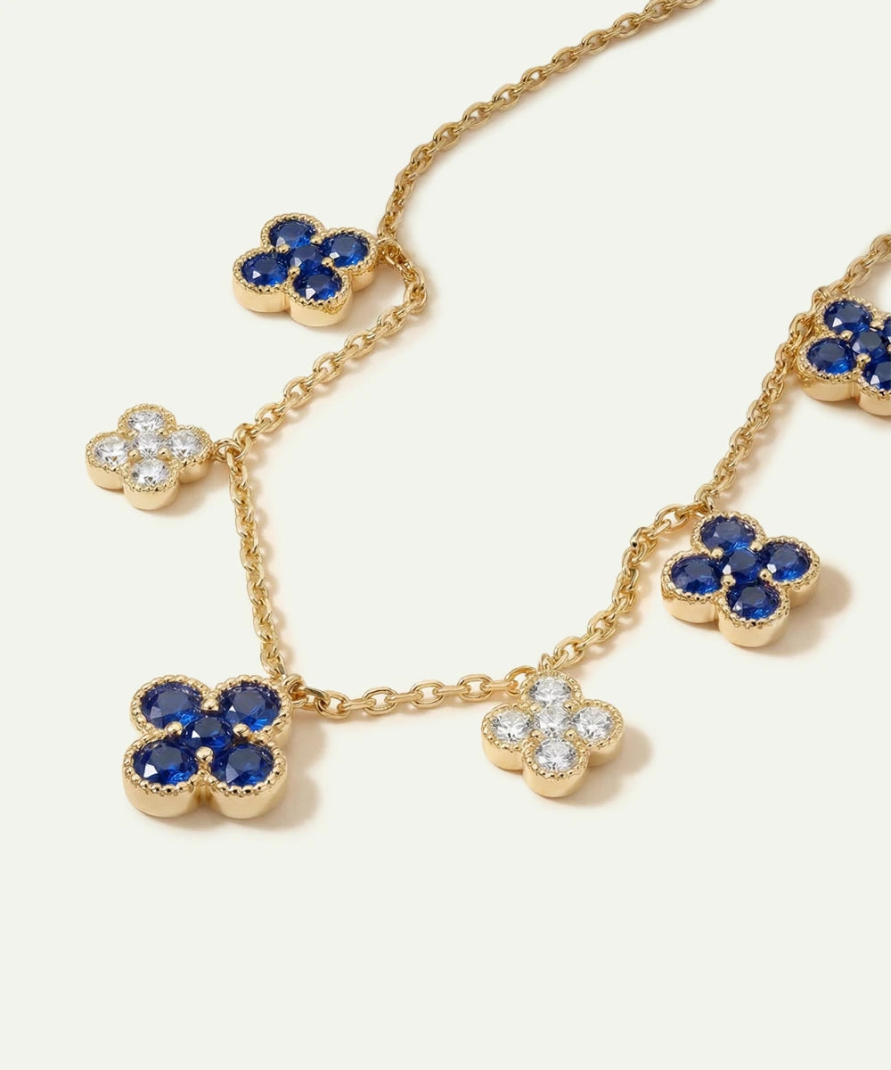 Gold necklace with blue and clear gemstone flower pendants on a white background