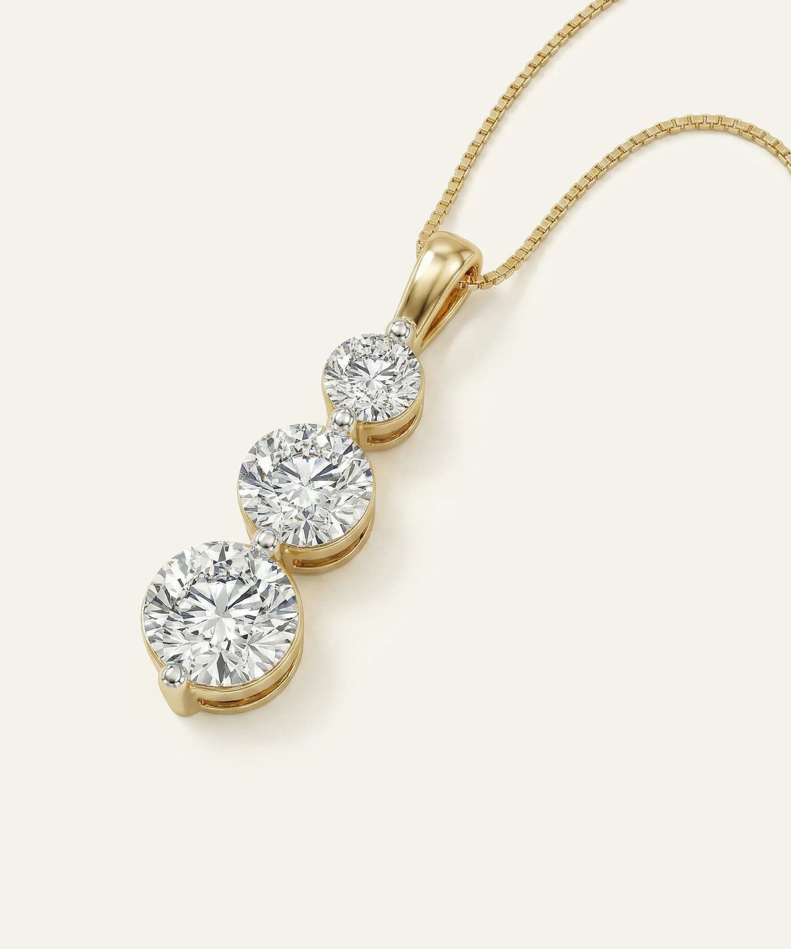 Gold necklace with three diamond pendants on a light beige background