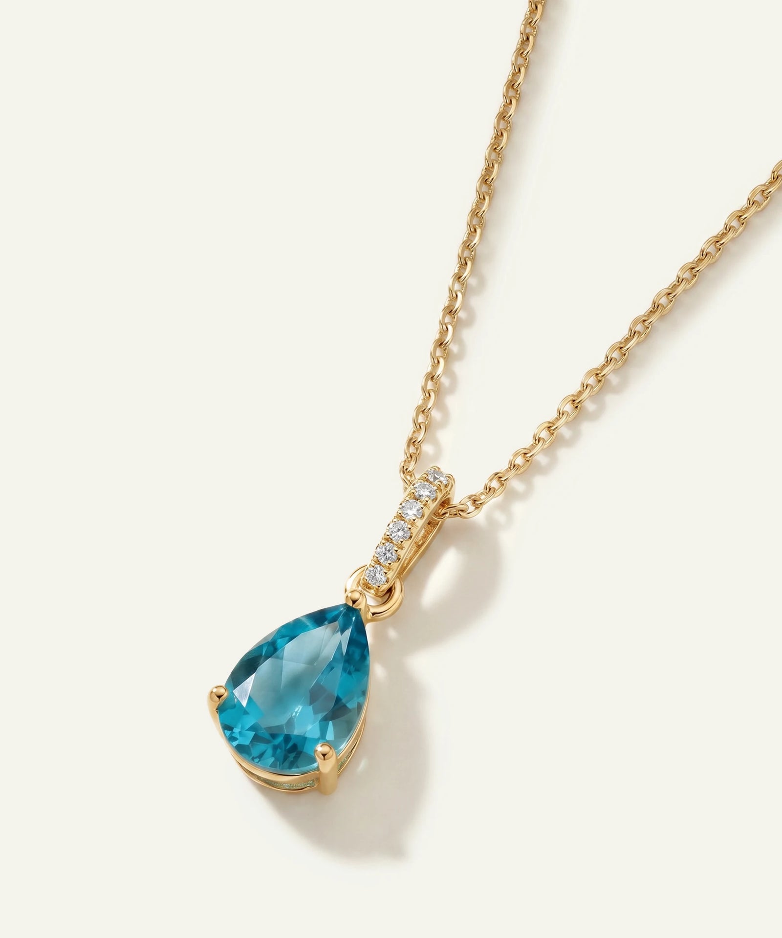 Gold necklace with a blue teardrop pendant on a white background