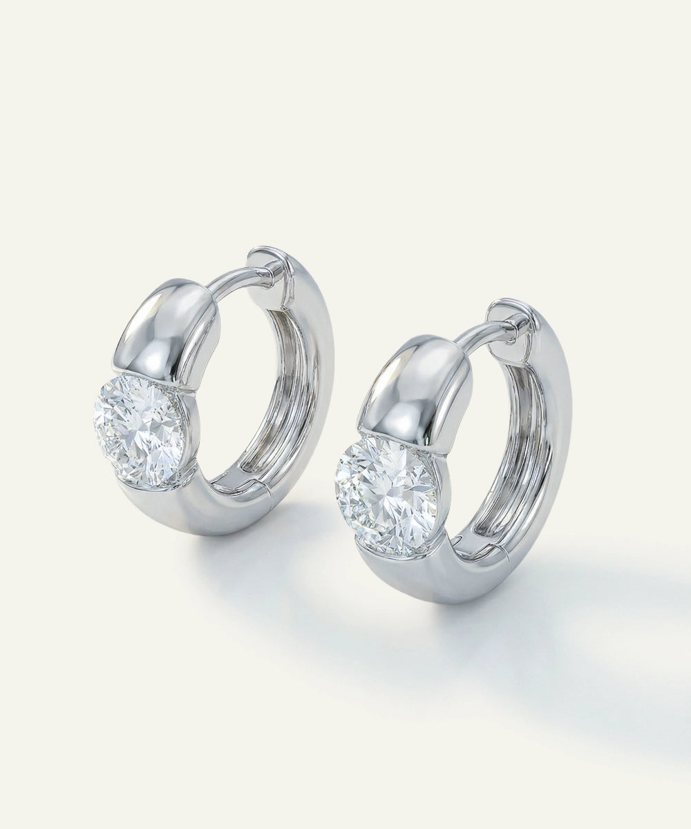Pair of silver hoop earrings with clear gemstones on a light gray background