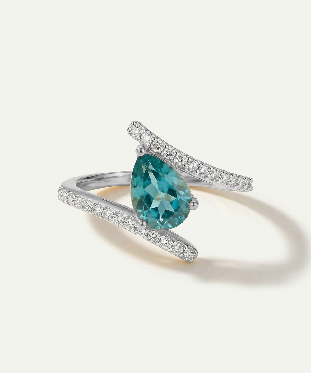 Ring with a pear-shaped blue gemstone and diamond-studded band on a white background