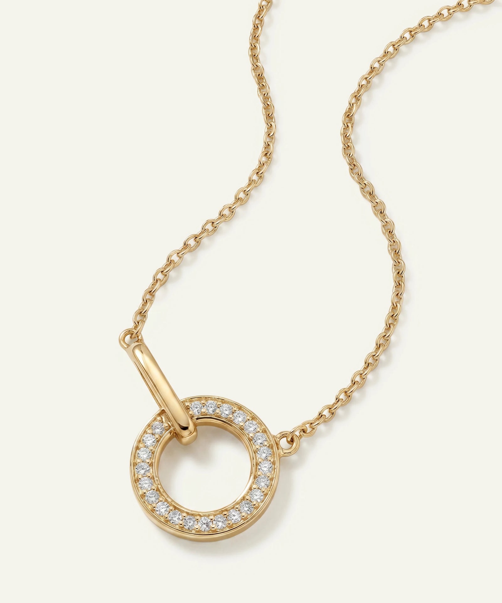 Gold necklace with a circular pendant on a light beige background