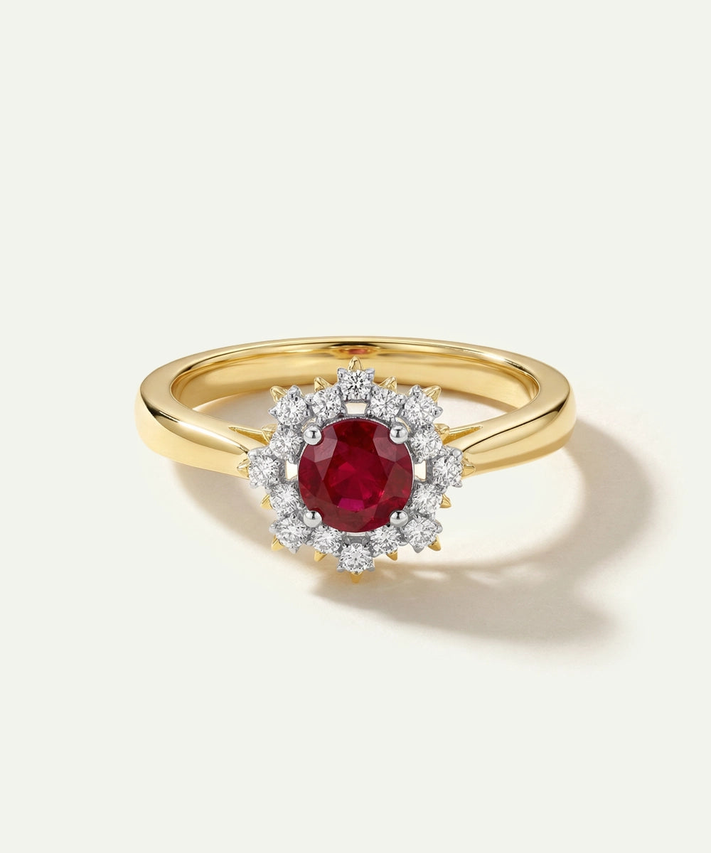 Gold ring with a red gemstone and diamond halo on a white background