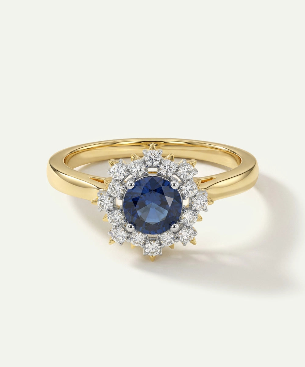 Gold ring with a blue gemstone and diamond halo on a white background
