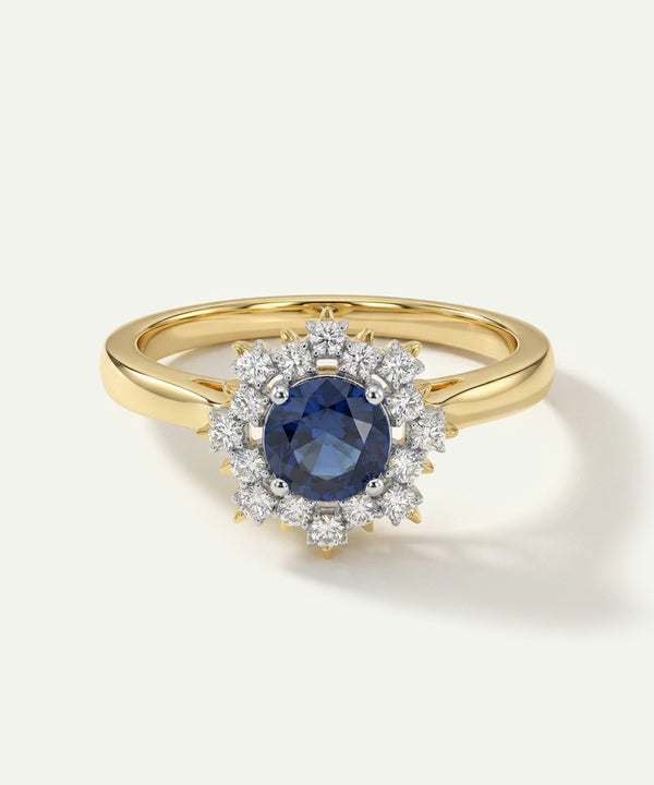 Gold ring with a blue gemstone and diamond halo on a white background