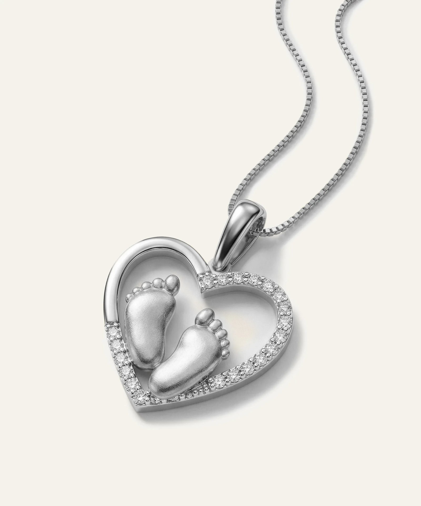 Silver heart-shaped pendant with baby feet design on a white background
