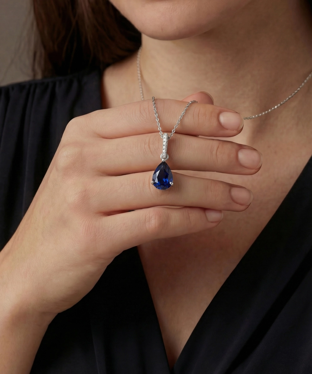 Person holding a silver necklace with a blue teardrop pendant