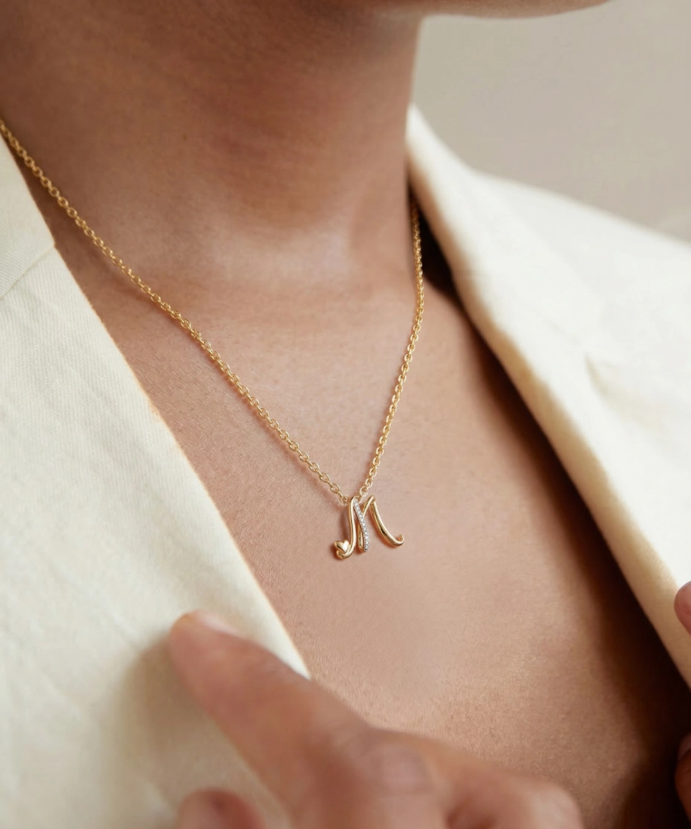 Gold necklace with a letter 'N' pendant worn by a person against a neutral background