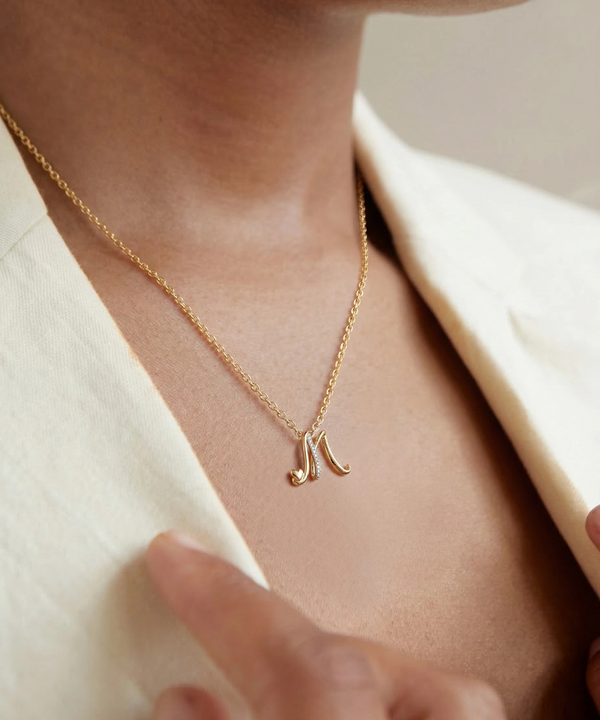 Gold necklace with a letter 'N' pendant worn by a person against a neutral background