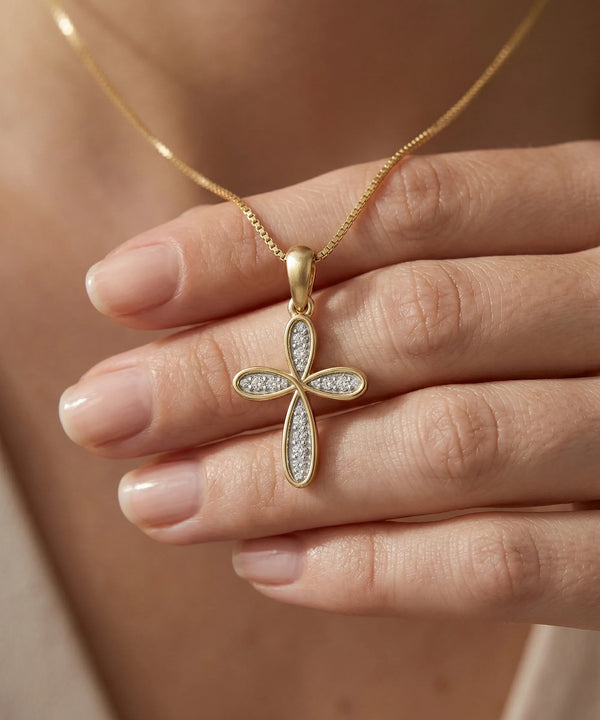 Gold cross pendant necklace held by a hand against a neutral background