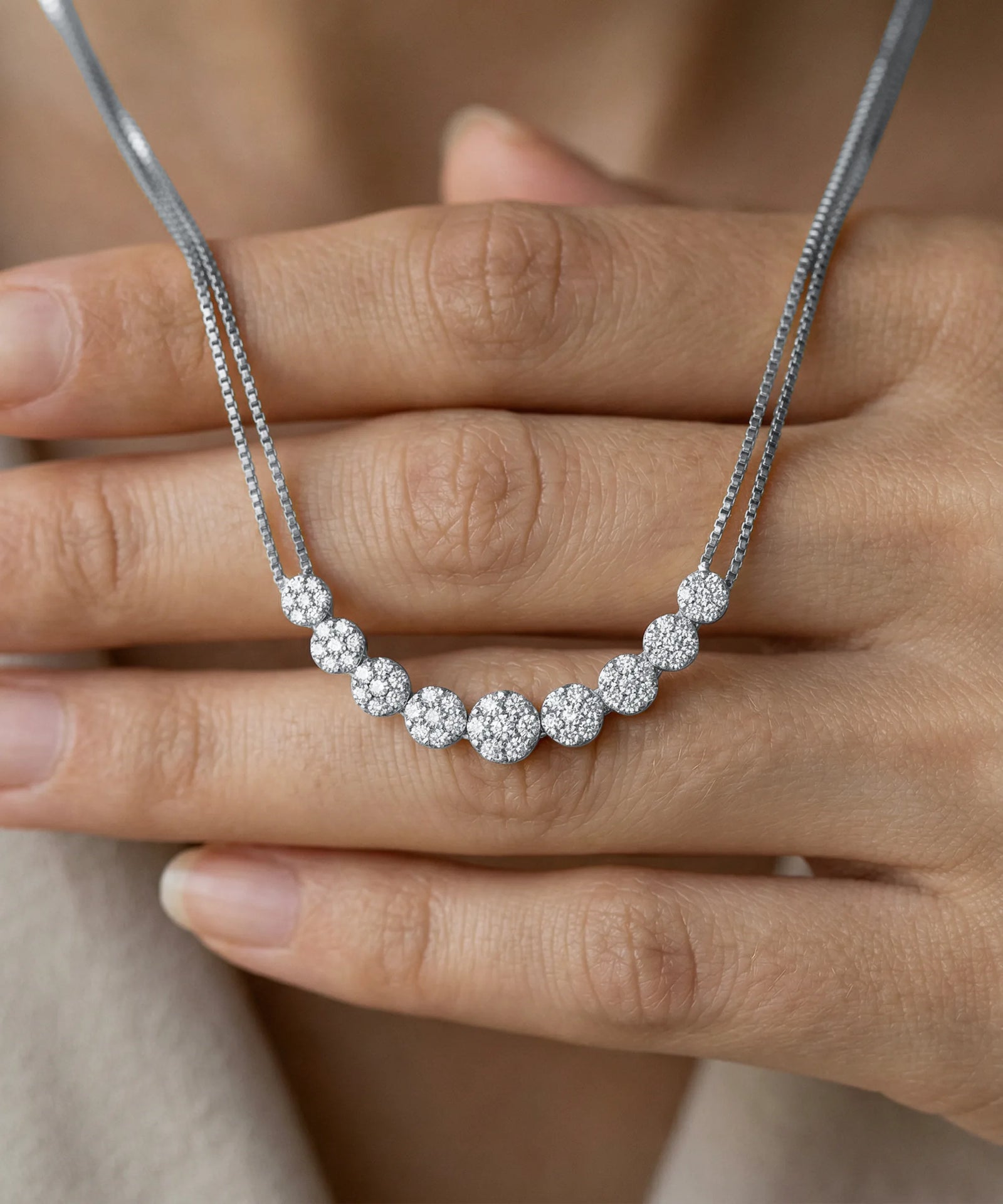 Silver necklace with round pendants held by a hand against a neutral background