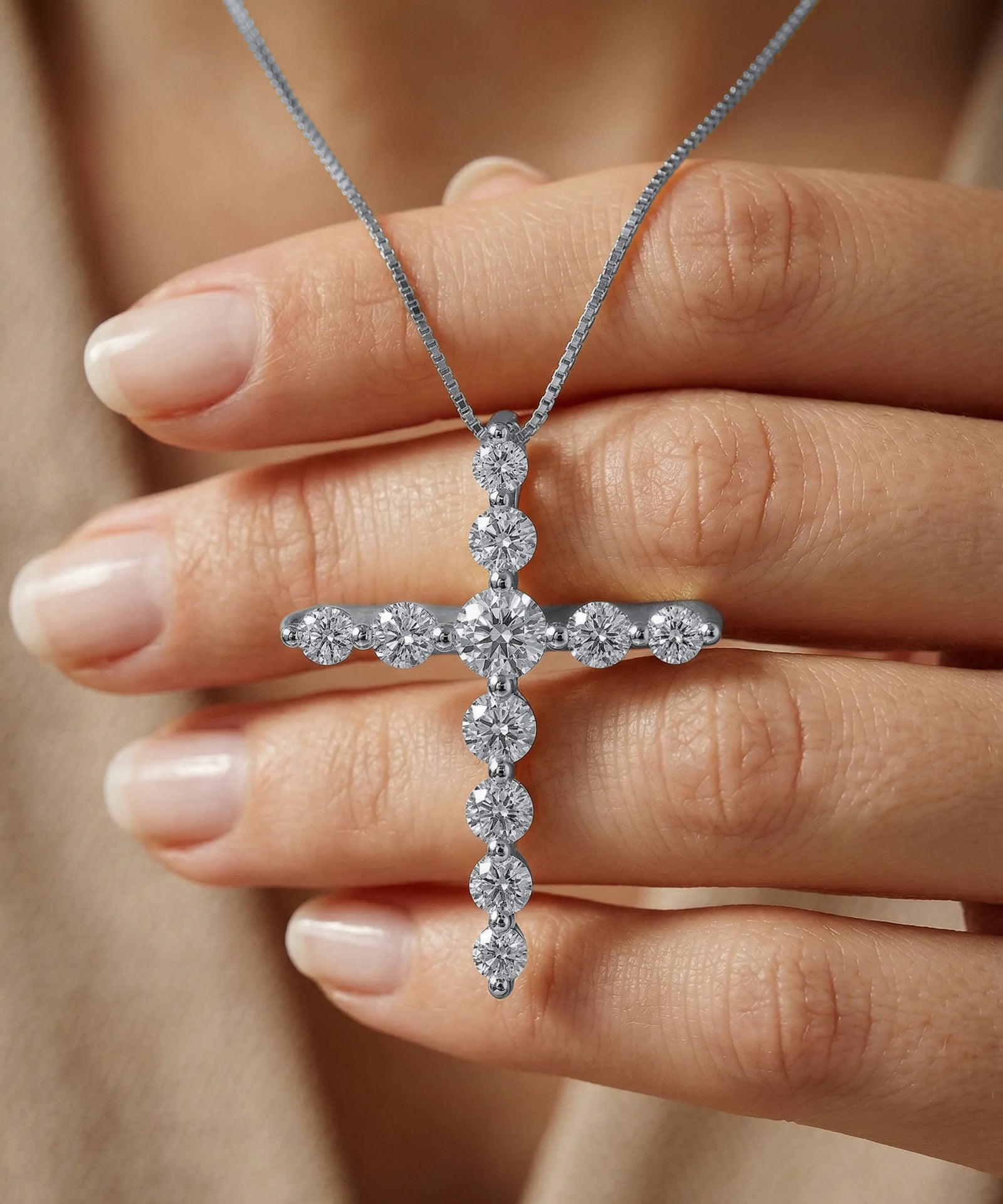 Diamond cross necklace held by a hand against a neutral background