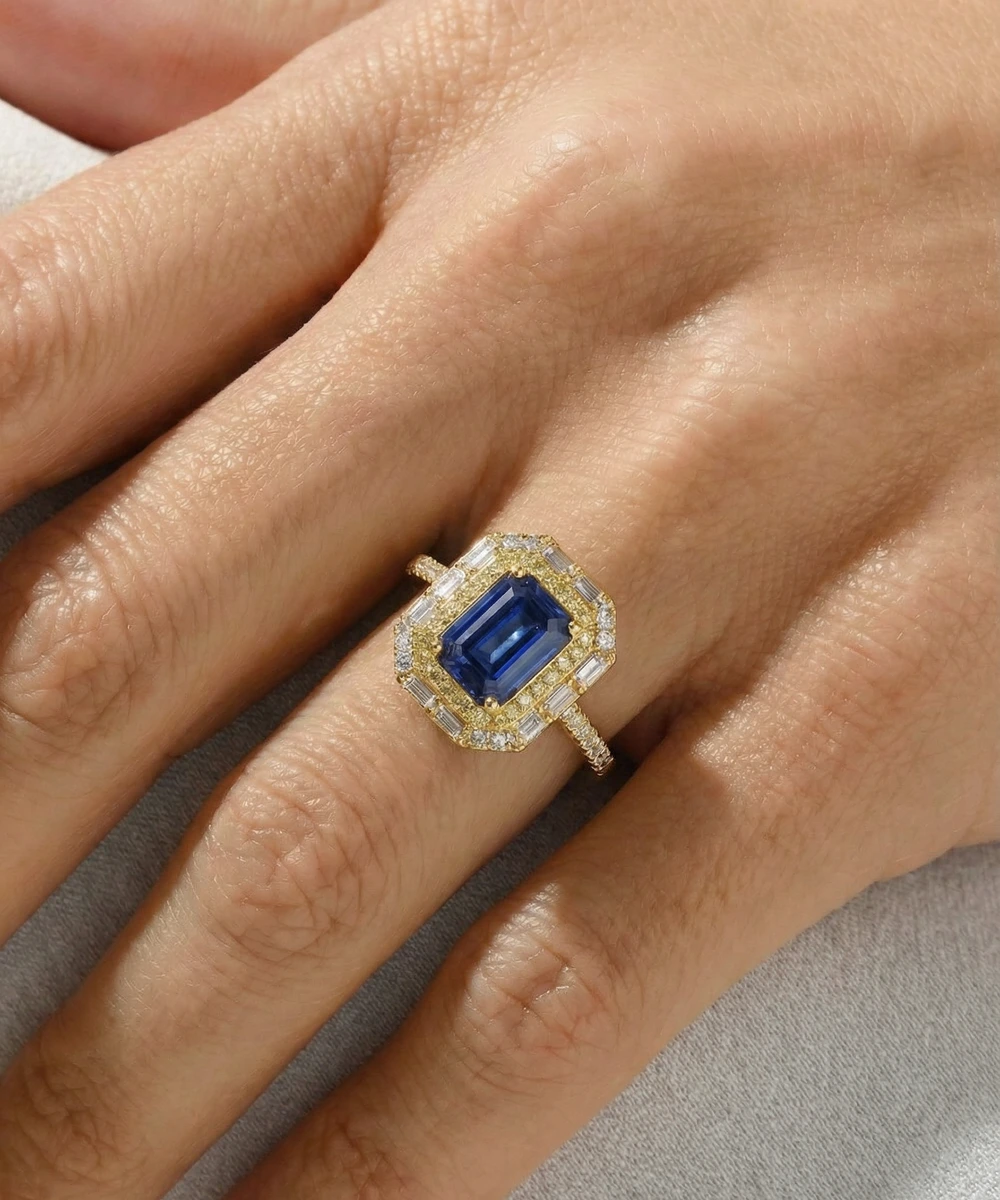Gold ring with a blue gemstone on a hand against a neutral background