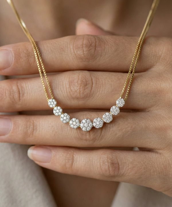 Gold necklace with diamond beads held by a hand against a neutral background