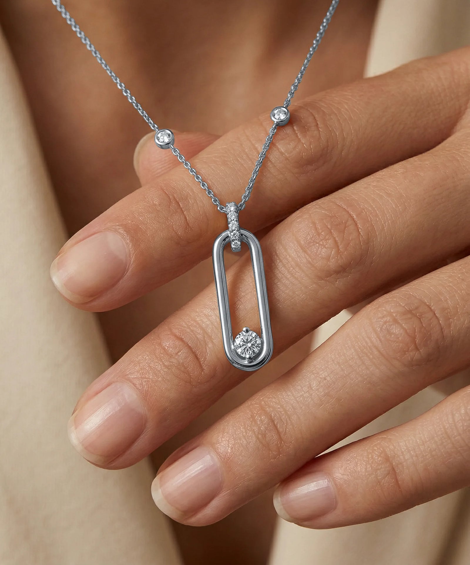 Silver necklace with a pendant held by a hand against a neutral background