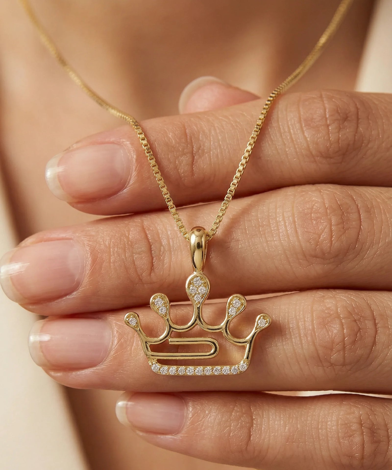 Gold crown-shaped pendant necklace on a hand